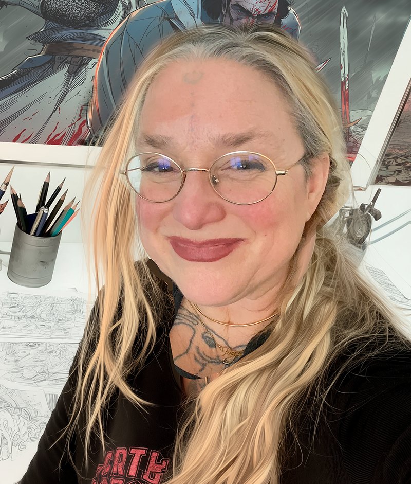 J. LuLu, artist and author, in her studio with comic artwork and pencils behind her.